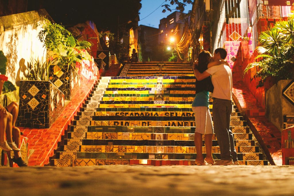 A couple embracing on the colorful, mosaic-tiled Escadaria Selarón (Selarón Steps) in Rio de Janeiro, Brazil, captured at night under warm streetlights
