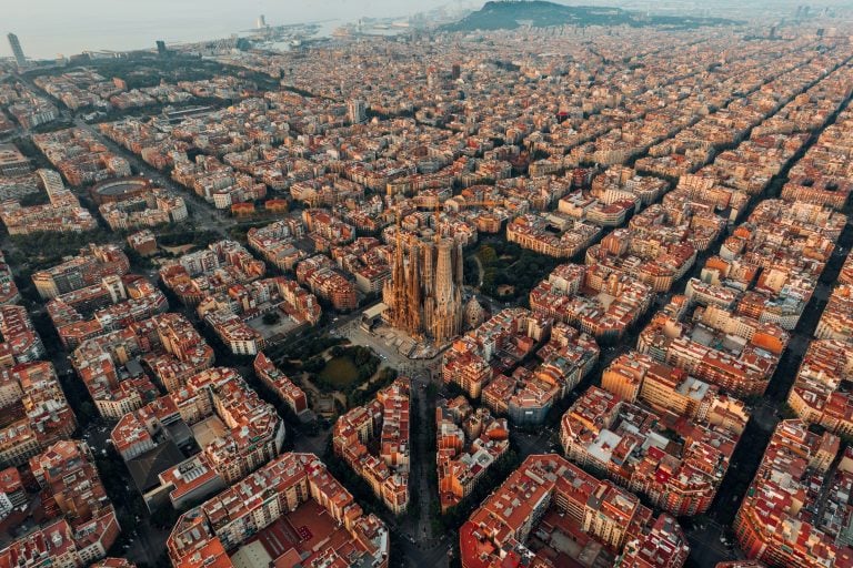 High aerial view of Barcelona, Spain, showing the Sagrada Familia basilica surrounded by the perfect, dense, geometric grid of the Eixample district buildings