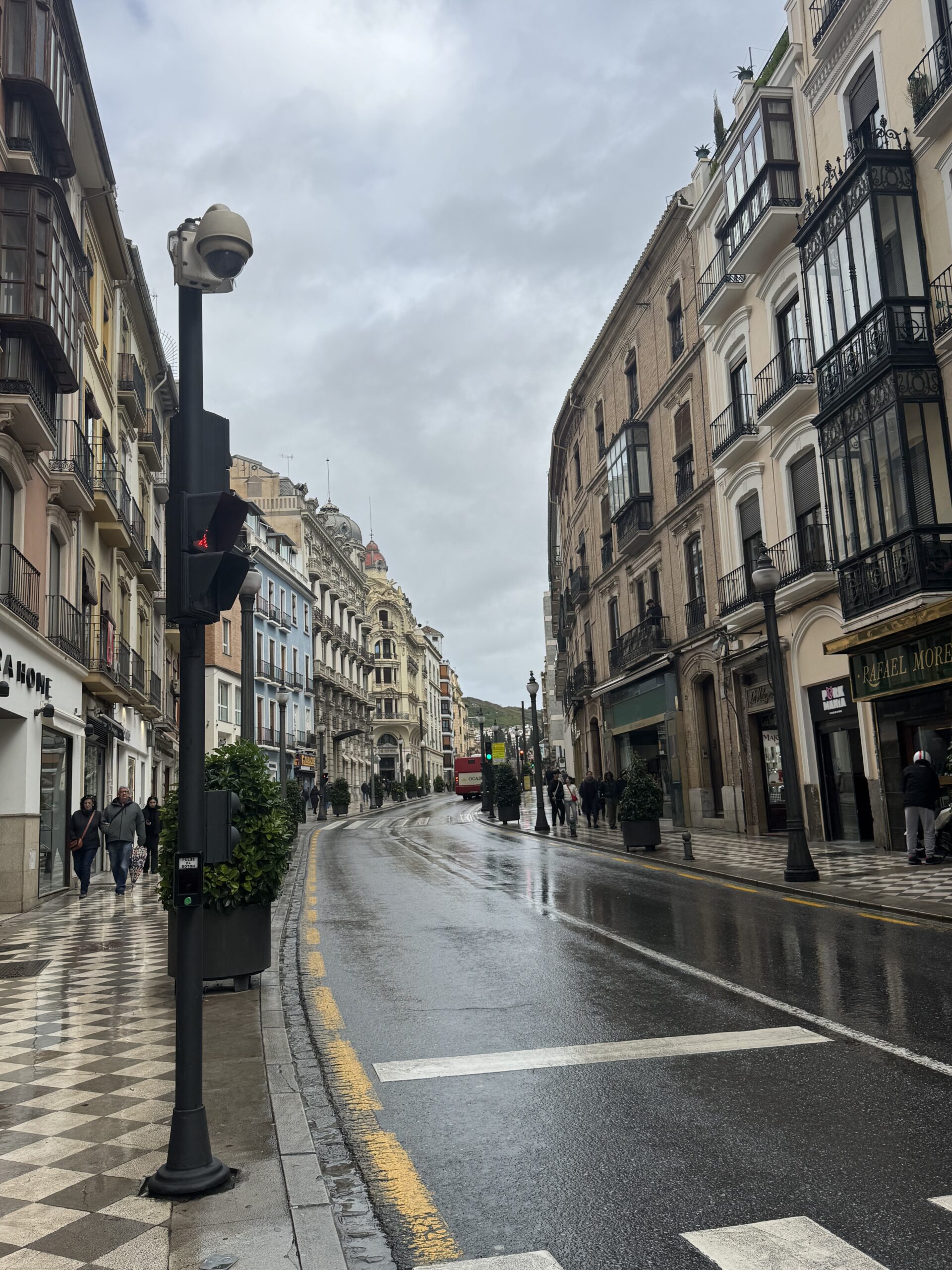 Wet stone pavement and 19th-century apartment buildings on a rainy afternoon in central Granada Spain.