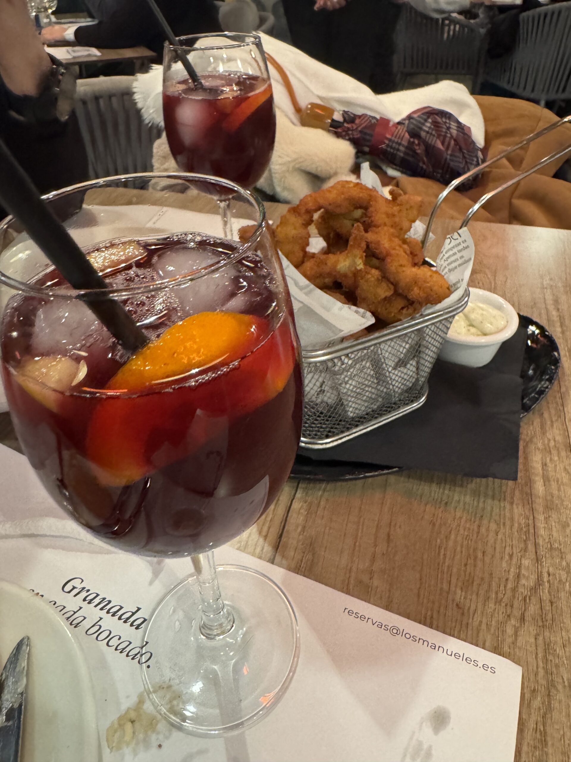 Two large glasses of iced red wine sangria with fresh citrus slices served next to a wire basket of golden fried calamari at Los Manueles restaurant.
