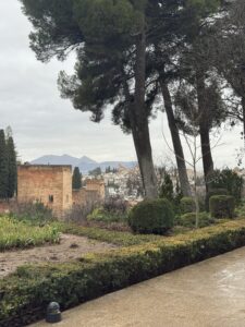 High angle view over the manicured hedge mazes of the Generalife gardens looking out toward the historic fortress walls under a cloudy sky.