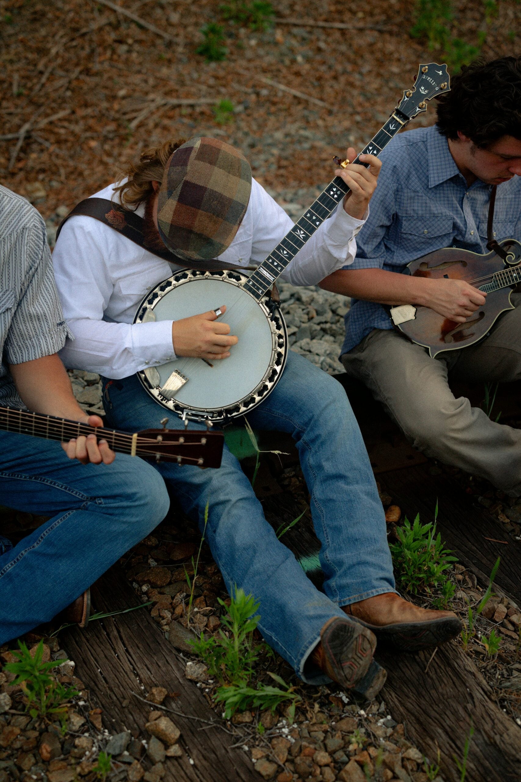 Acoustic bluegrass musicians playing banjo, guitar, and mandolin together outdoors