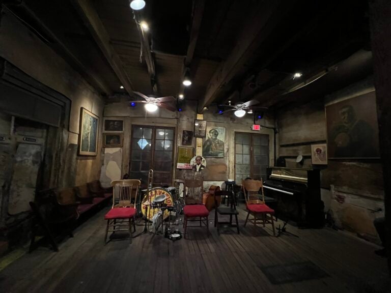 An intimate New Orleans music room with piano, double bass, drum kit and chairs